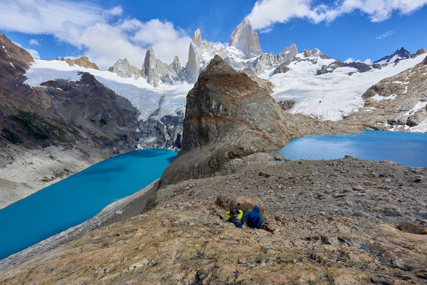 Patagonia, Argentina: A couple in mountain gear rests on rocks with view to Lago de los Tres and Mount Fitz Roy.